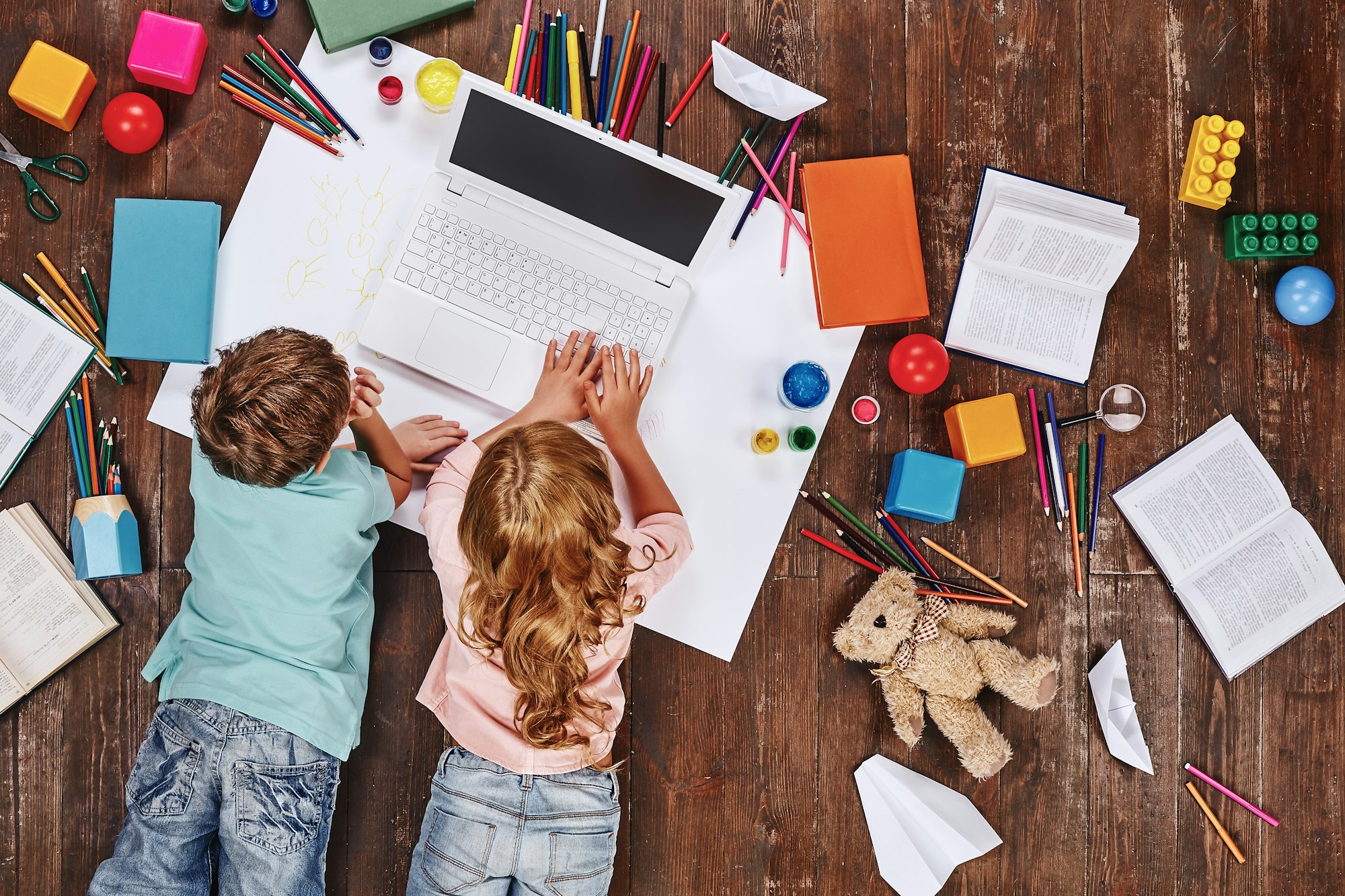 There are so many things. Children lying near books and toys, while playing on toy computer